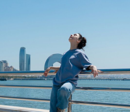 “깊은 잠이 주는 힘, 내 일상에 스며드는 건강 수면 루틴” Woman enjoys the sun with water and city views.